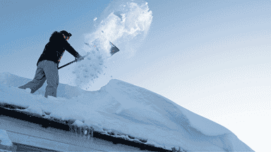  Residential snow removal worker clearing snow from roof for safe and efficient home service.
